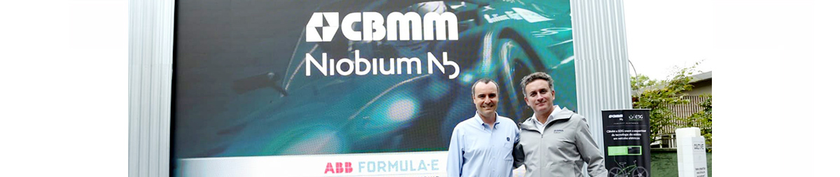 dois homens em frente a placa da CBMM